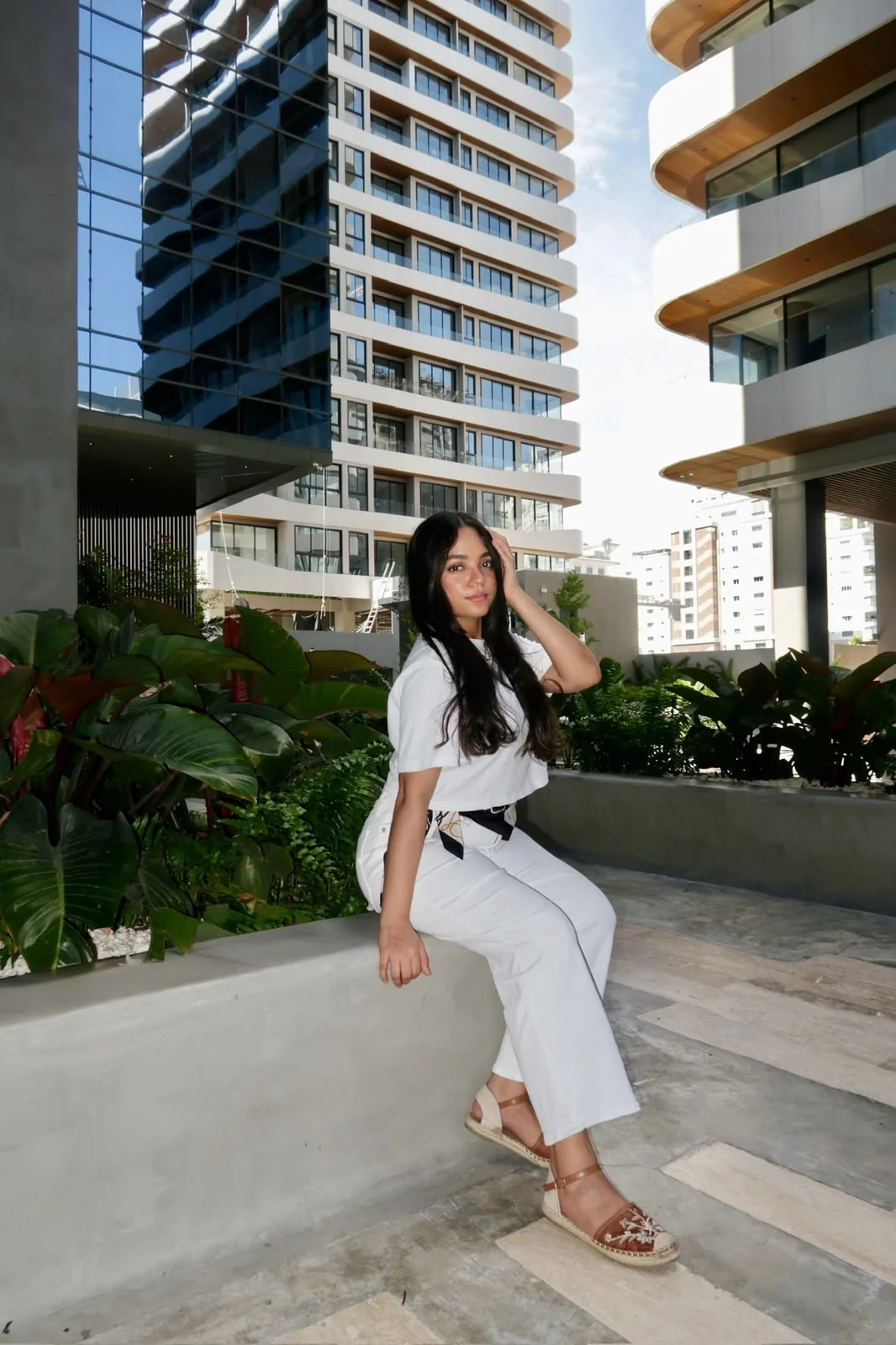 Wileini con conjunto blanco, sentada en un espacio urbano con jardines
